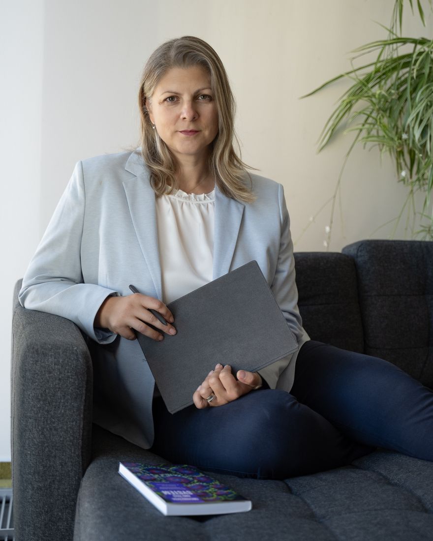 Žena v svetlom saku sedí na pohovke so zápisníkom